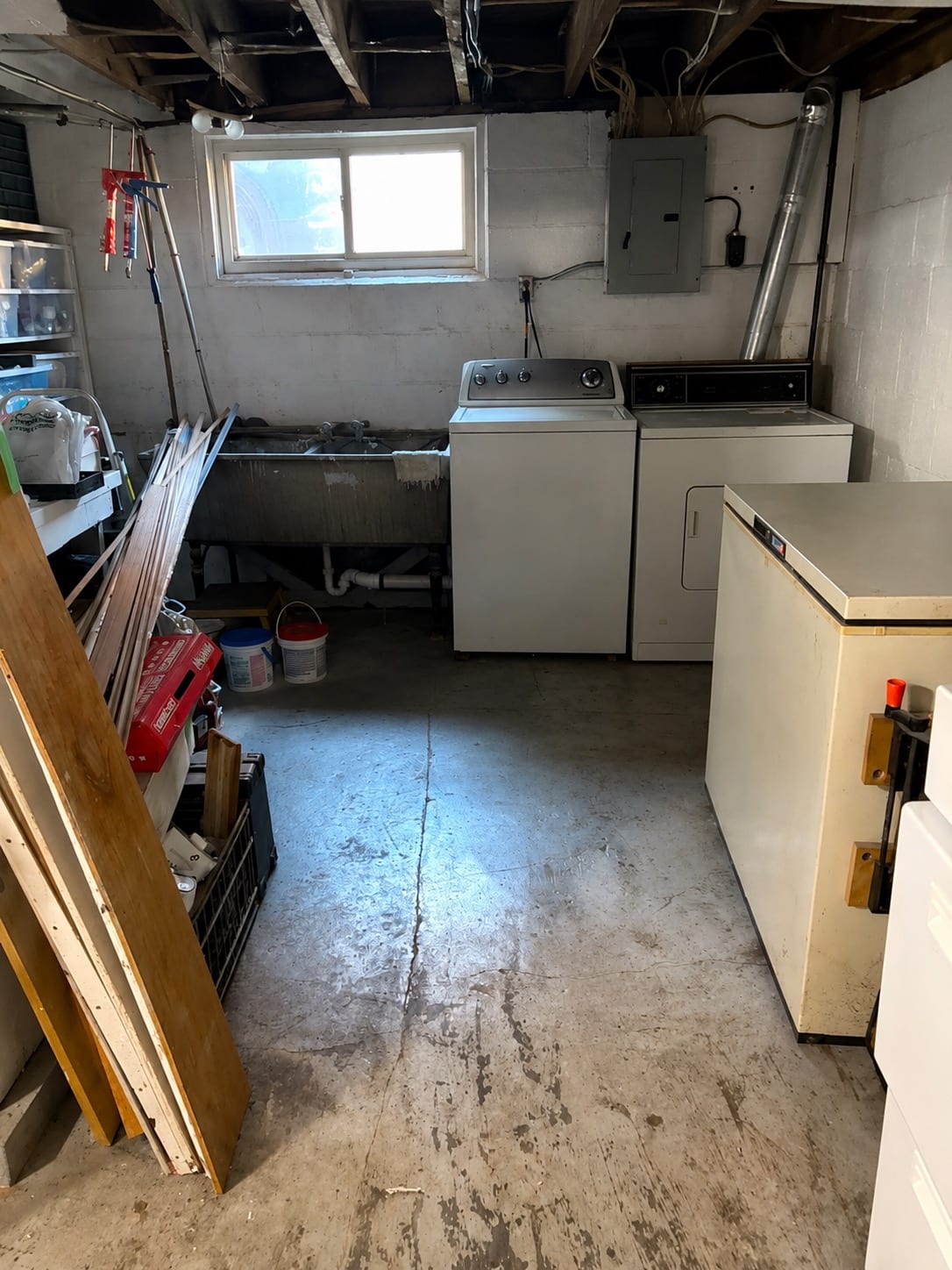 Basement laundry area before work: uncoated concrete floor with visible staining and cracking beside a washer, dryer and freezer