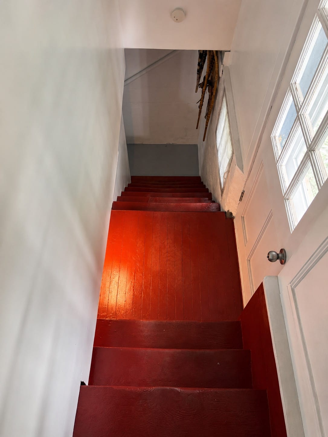 The same basement stairs after work: evenly repainted red treads and landing with clean white stairwell walls