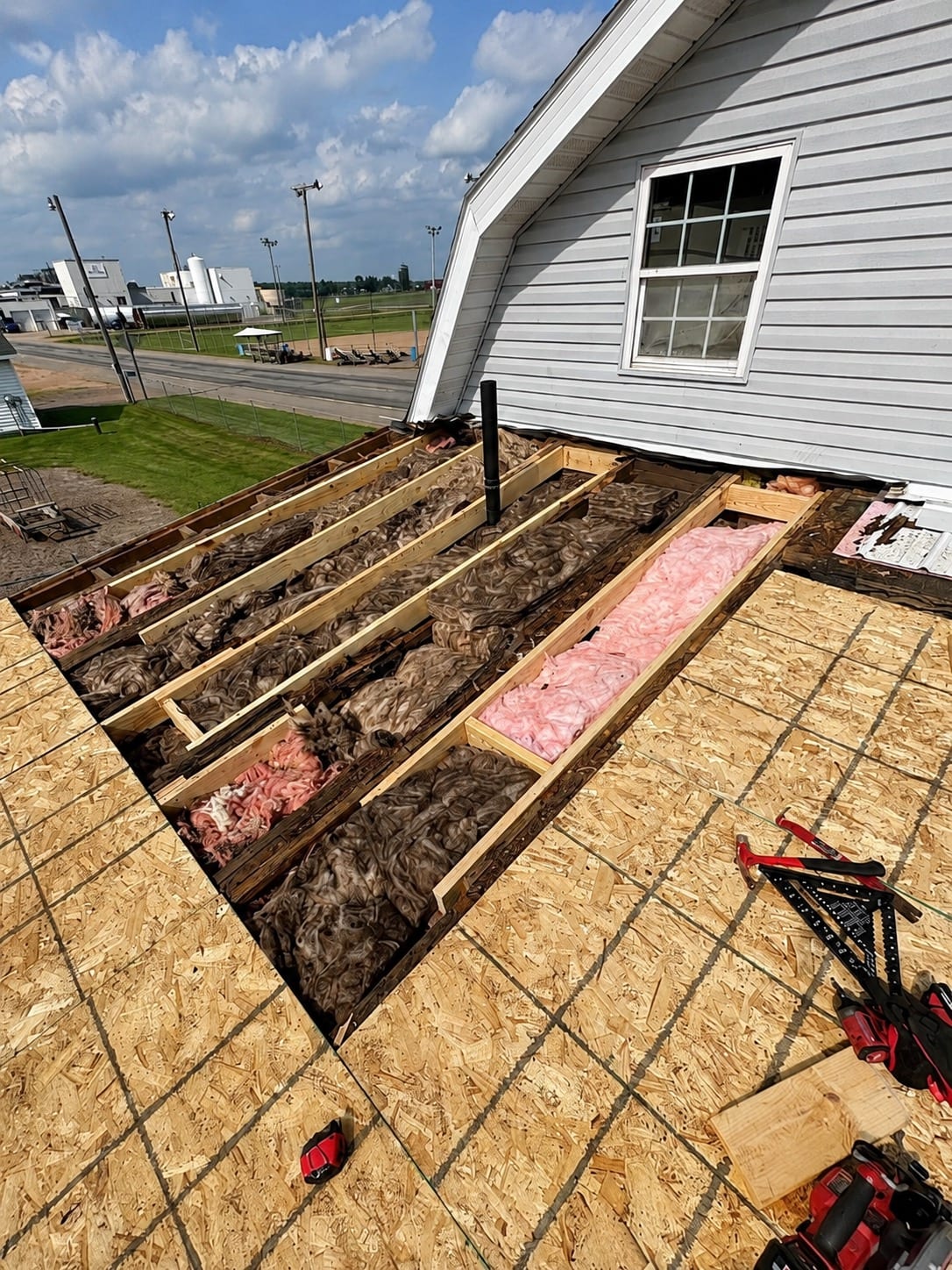 Roof during tear-off: new sheathing installed across most of the slope with one bay left open, exposing rafters and old insulation