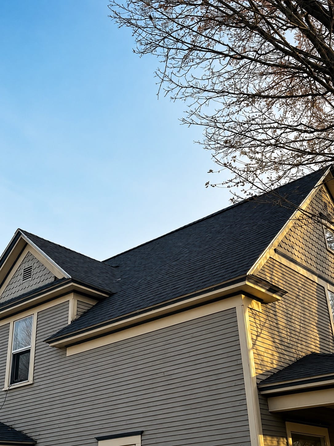 A completed charcoal shingle roof on a two-story home with cream trim