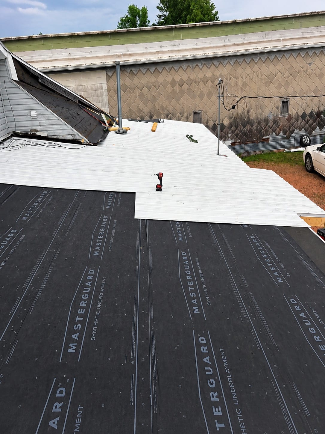 Roof mid-installation with metal panels being laid over synthetic underlayment and a section of old roofing still exposed