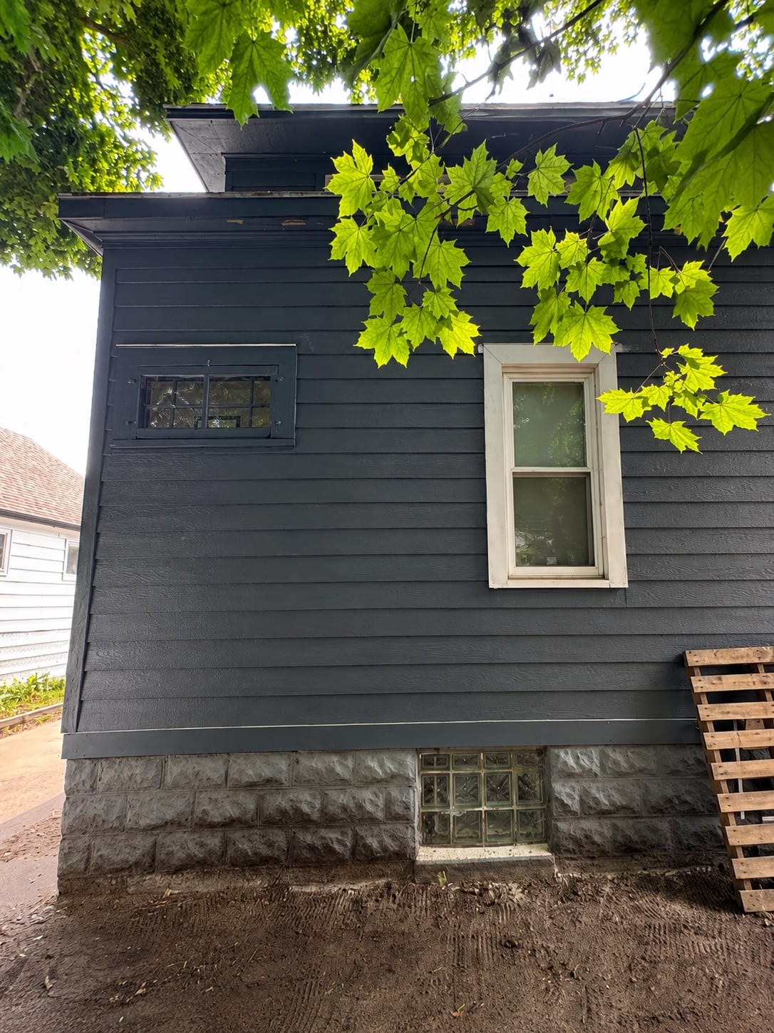 Finished dark navy siding wall with a trimmed basement window above freshly graded soil at the foundation